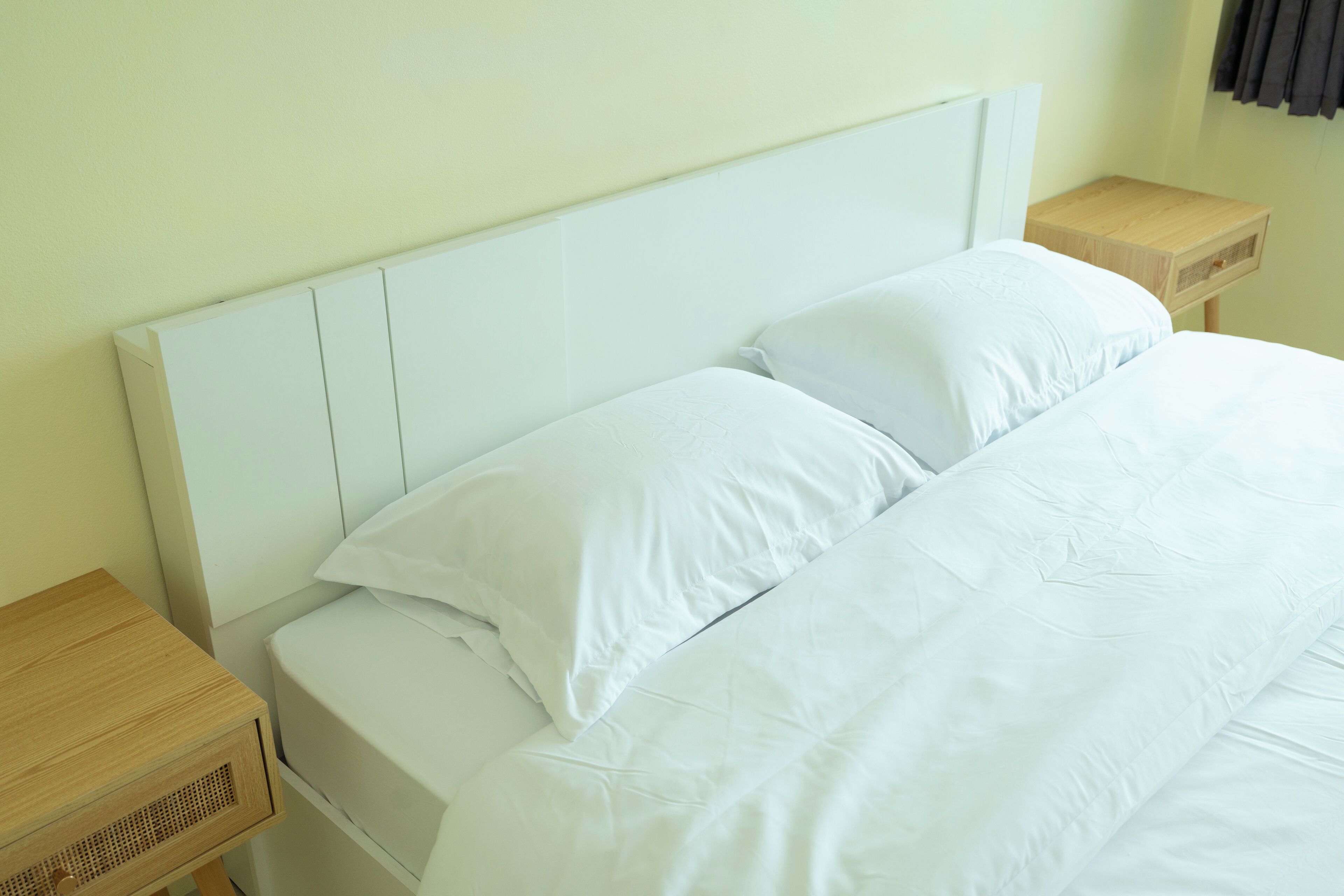 A neatly made bed with white linens and a wooden headboard in a room with light-colored walls.