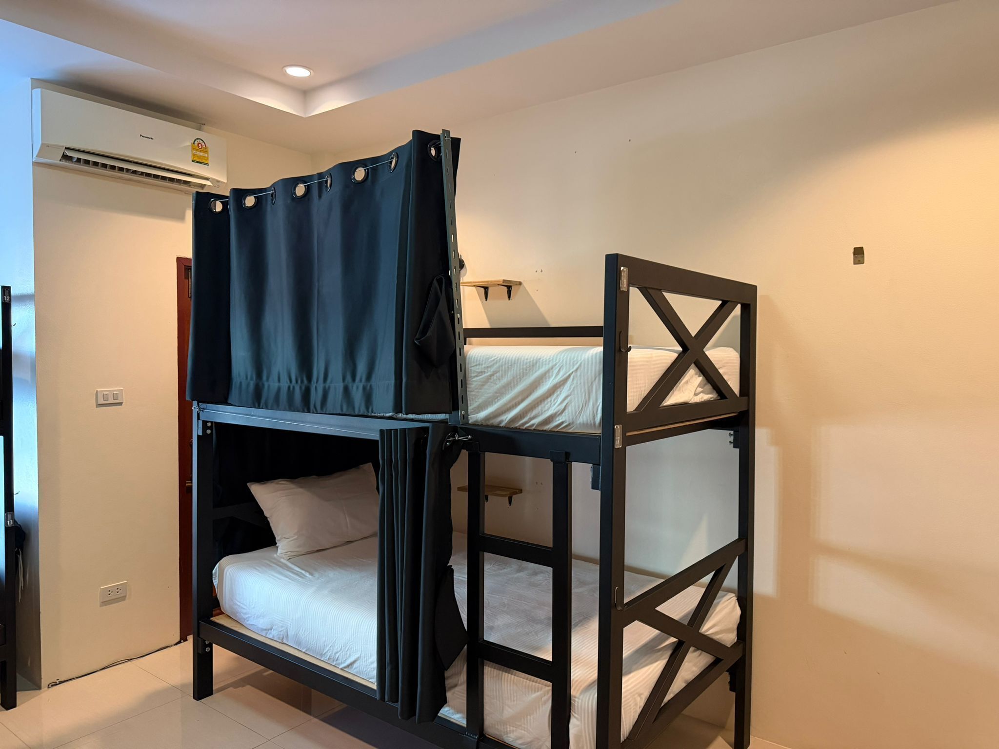 Una cama litera con cortina, un aire acondicionado instalado en la pared y una lámpara de noche.