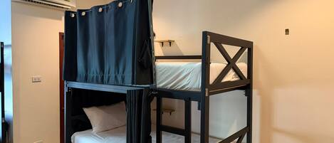 Una cama litera con cortina, un aire acondicionado instalado en la pared y una lámpara de noche.