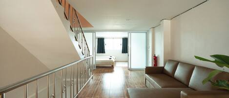 A spacious living area with a wooden floor, a brown leather sofa, and a staircase with metal railings.