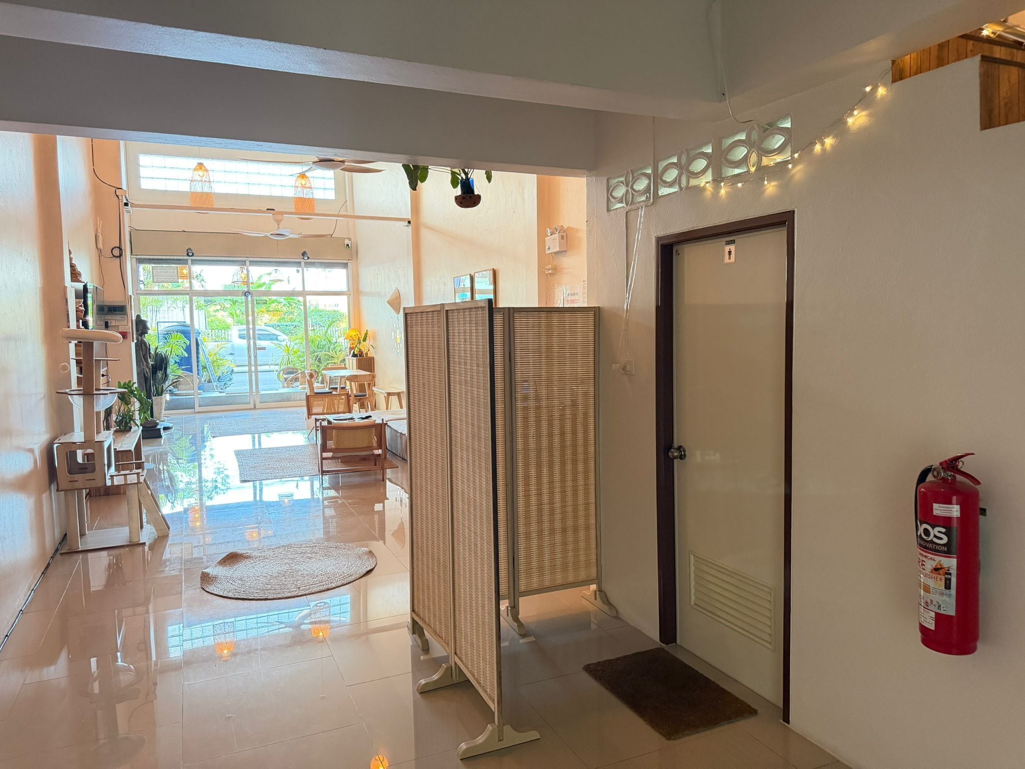 Vestíbulo de hotel con mostrador de recepción, extintor, puerta de vidrio y vistas al exterior a través de amplias ventanas.