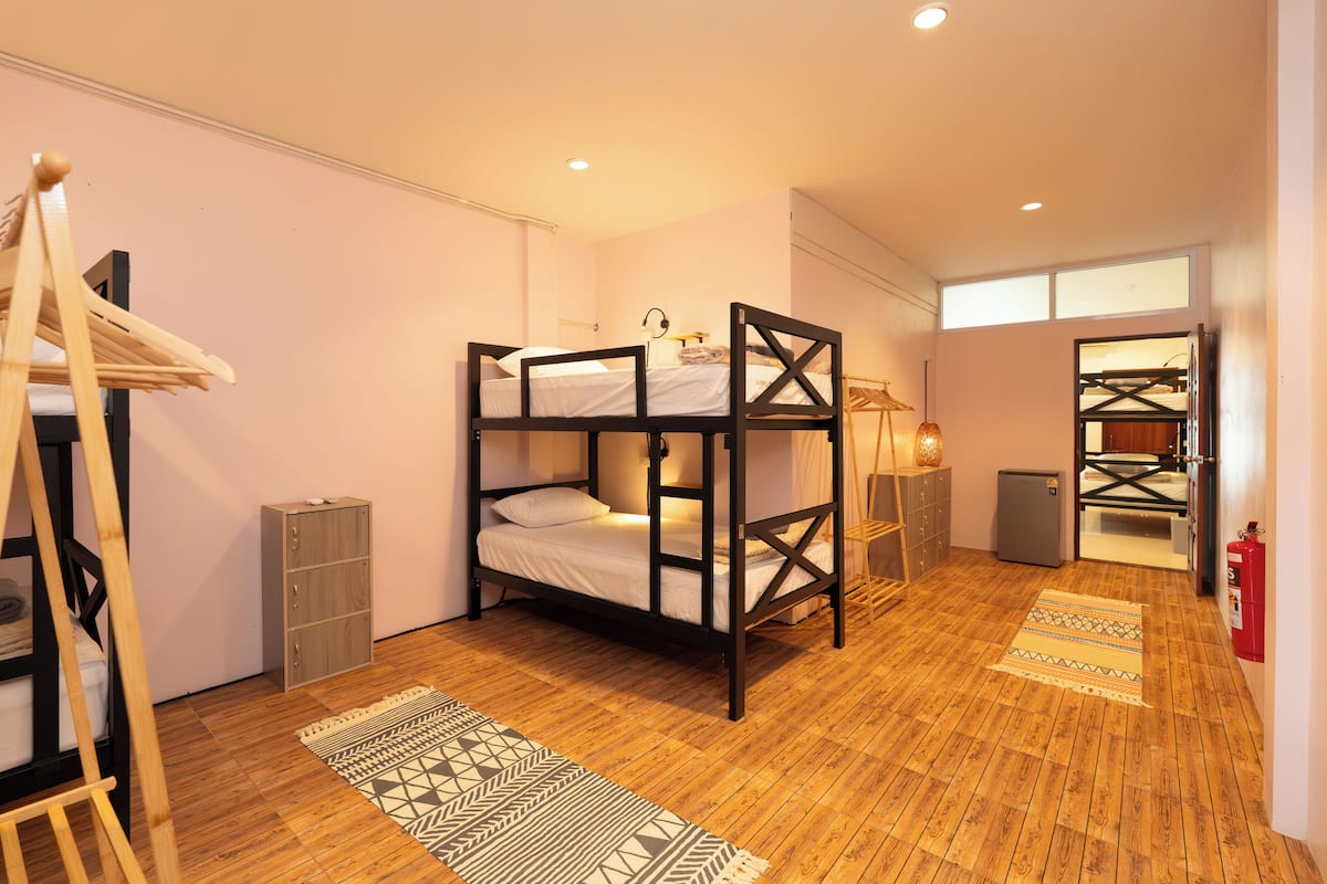 A bunk bed room with a wooden floor, a small cabinet, a lamp, and a fire extinguisher.
