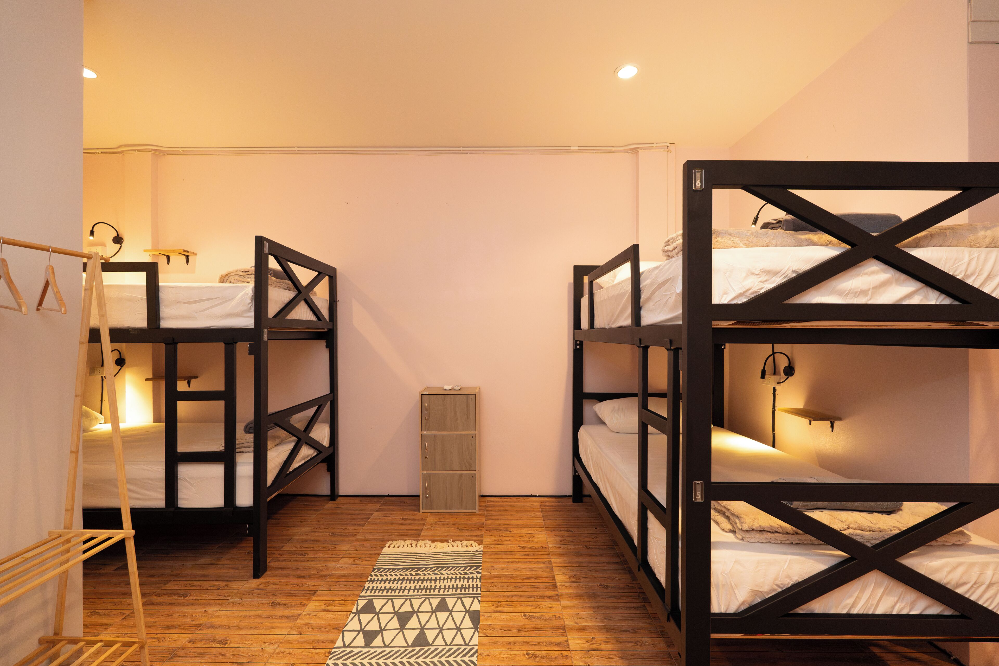 A dormitory room with bunk beds, a wooden floor, a patterned rug, and a small cabinet.