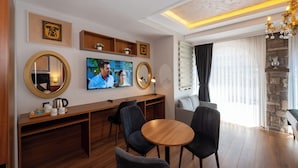 A modern hotel room with a wooden dining area, a TV mounted on the wall, and a stone accent wall.