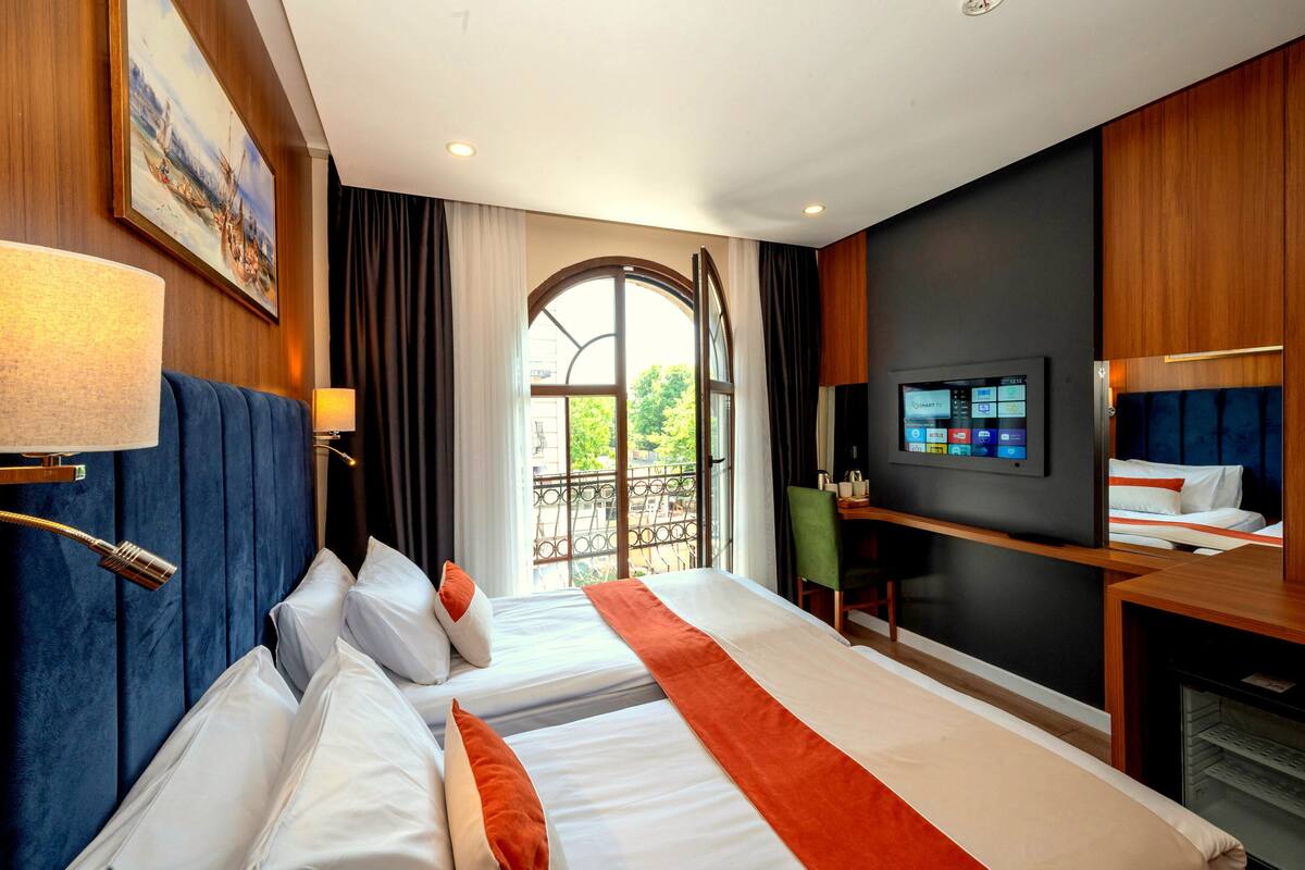 Une chambre d’hôtel avec deux lits, une télévision, un bureau et une grande fenêtre donnant sur un beau paysage.