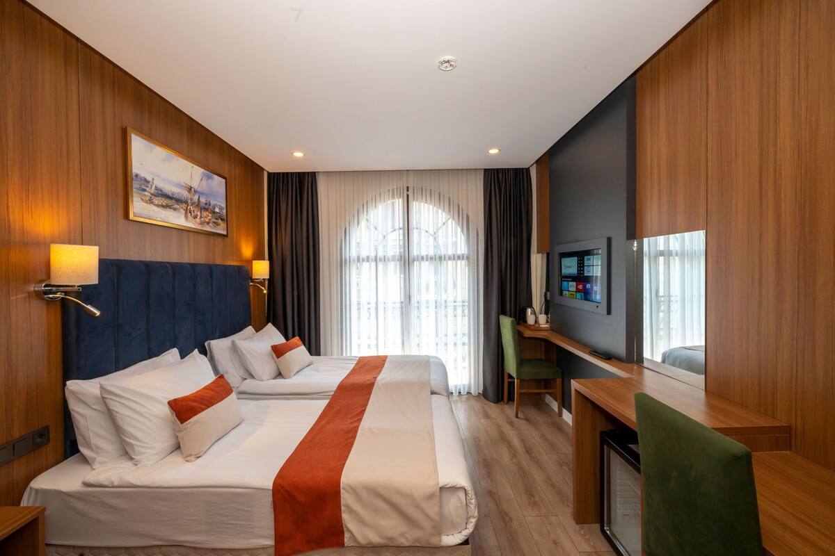 Une chambre d’hôtel avec deux lits, un bureau, une chaise, une télévision et une fenêtre avec des rideaux.