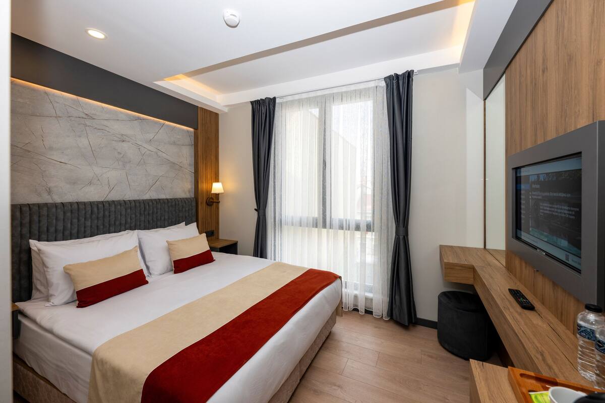 Une chambre d’hôtel moderne avec un grand lit, une télévision, un bureau et une fenêtre avec des rideaux.