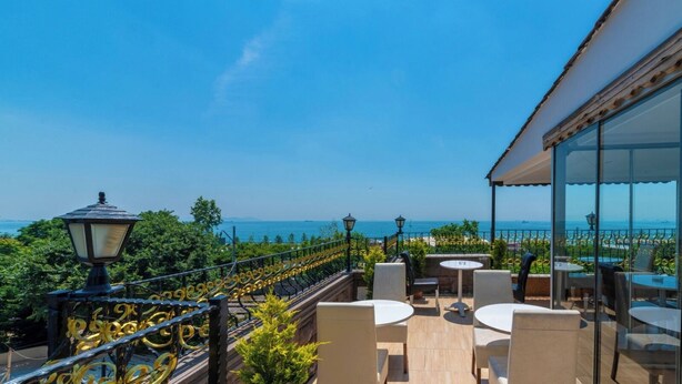 An outdoor terrace with a view of the sea, featuring outdoor seating and a railing with decorative elements.