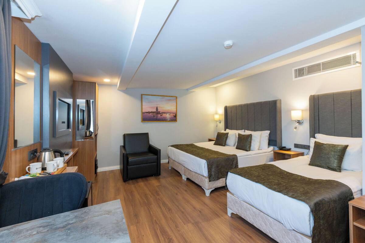 Une chambre d’hôtel avec deux lits, un bureau avec une chaise, une machine à café et un tableau au mur.