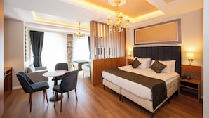 A hotel room with a large bed, a dining area with a table and chairs, a chandelier, and a view of the outdoors.