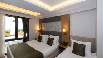 Ein Hotelzimmer mit zwei Betten, einem großen Fenster mit Vorhängen, einem hölzernen Kopfteil und einem Nachttisch mit Lampe.