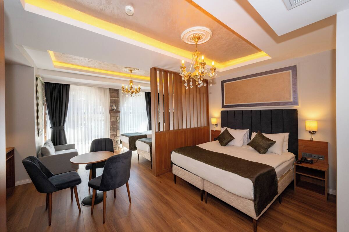 Une chambre d’hôtel avec un grand lit, un bureau, deux chaises, un lustre et une table de chevet avec une lampe.