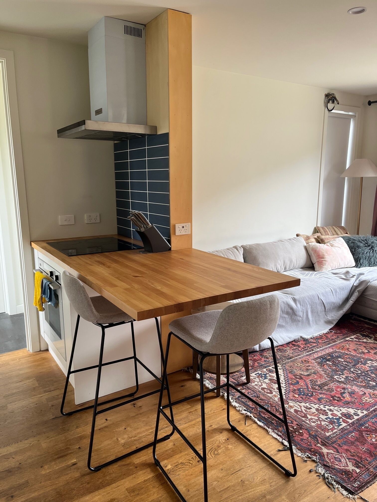Una cocina compacta con una mesa de madera, dos taburetes altos y un horno empotrado.