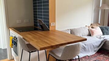 Una cocina compacta con una mesa de madera, dos taburetes altos y un horno empotrado.