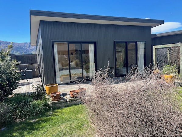 A modern house with large sliding glass doors, a patio with potted plants, and a view of mountains. - Lake Hawea Little Maude Snug (Lake Hāwea)