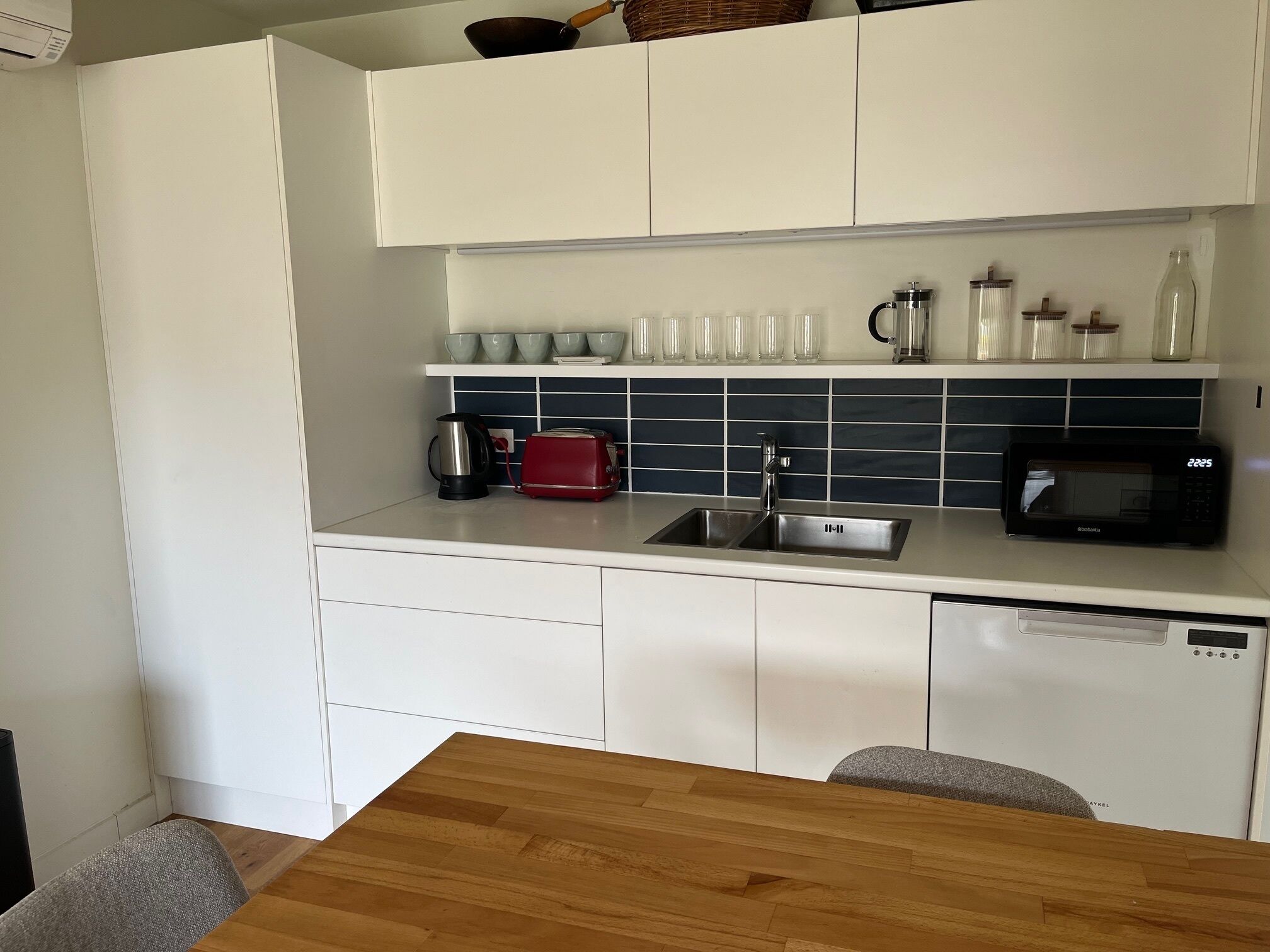 Una cocina moderna con armarios blancos, un microondas negro, un tostador rojo y una cafetera.