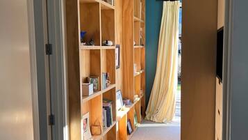 Un corridoio con una libreria in legno piena di libri e oggetti decorativi, che conduce a una stanza con un'ampia finestra e una tenda.