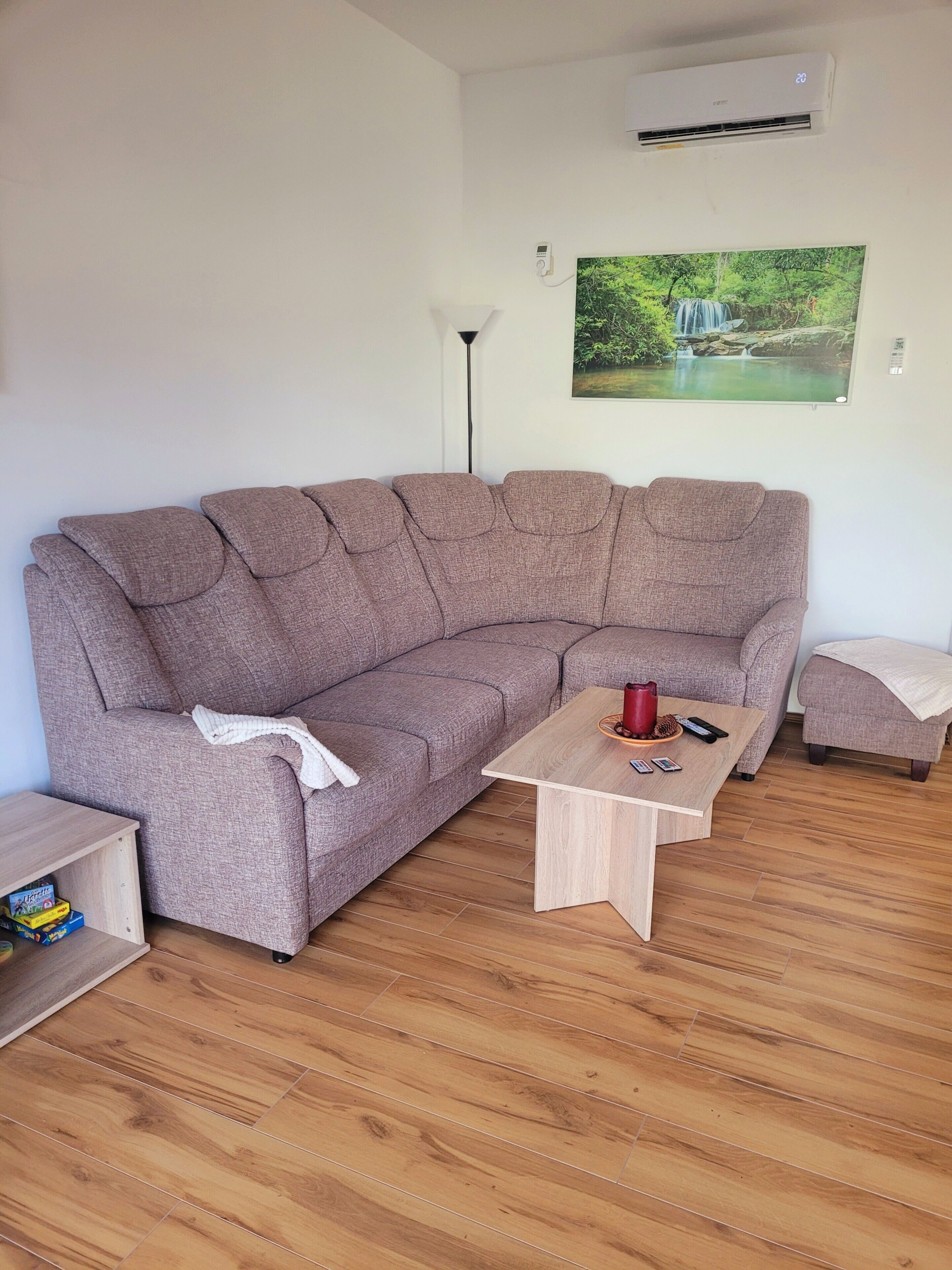 A modern living room with a sectional sofa, a wooden coffee table, a small ottoman, a floor lamp, and a wall-mounted air conditioner.