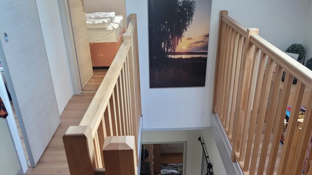 Eine Holztreppe mit Handlauf, die zu einem Schlafzimmer mit Bett und Fenster führt.