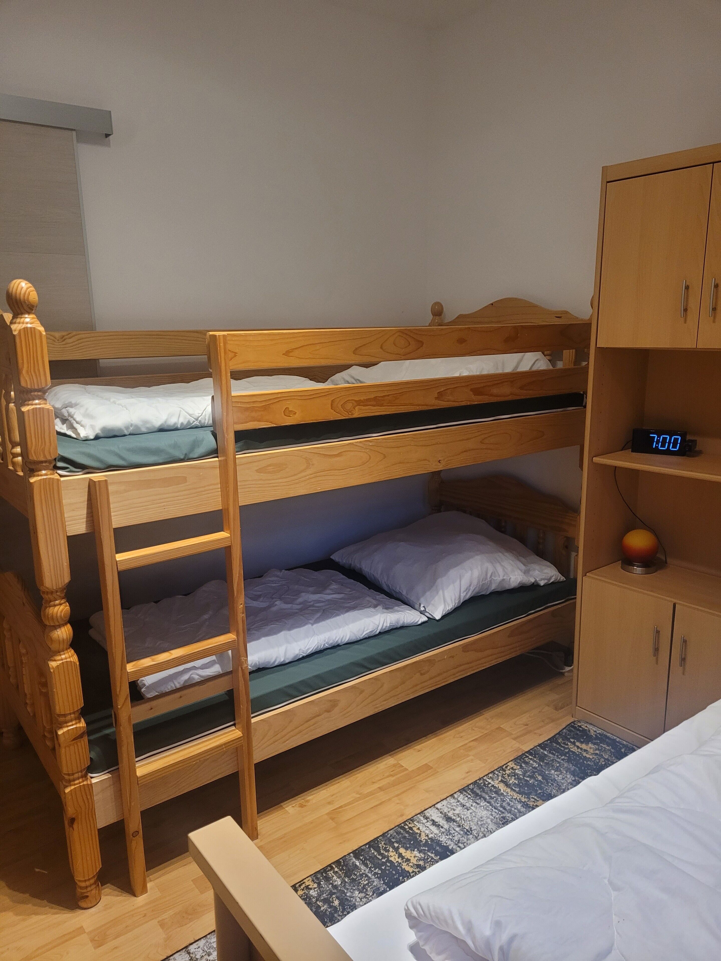 En køjeseng med træramme, en lille hylde med et ur, og en garderobe med to døre.