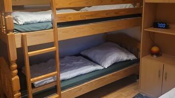 En køjeseng med træramme, en lille hylde med et ur, og en garderobe med to døre.