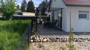 Ein Haus mit rotem Ziegeldach, einer überdachten Terrasse mit Gartenmöbeln und einer Steinsäule.