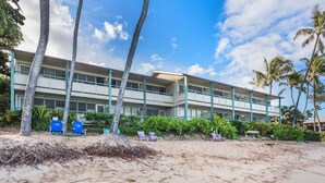 Ein Strandhotel mit mehreren Balkonen, Palmen und Liegestühlen.