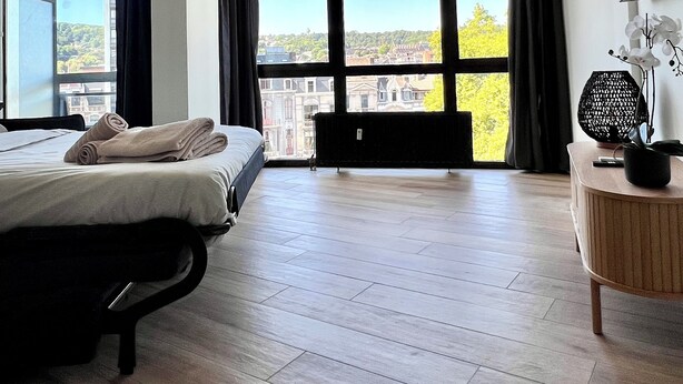 Ein geräumiges Schlafzimmer mit einem großen Bett, einem Deckenventilator und Blick auf eine Stadtlandschaft durch große Fenster.