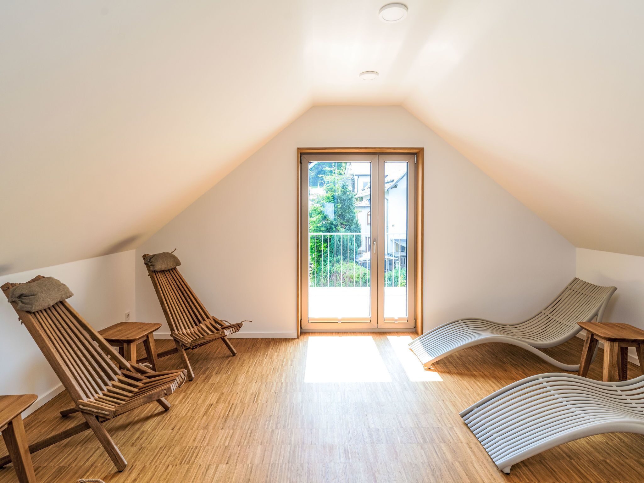 Ein geräumiges Dachzimmer mit Holzboden, zwei Holzloungesesseln und einer großen Schiebetür zu einem Balkon.