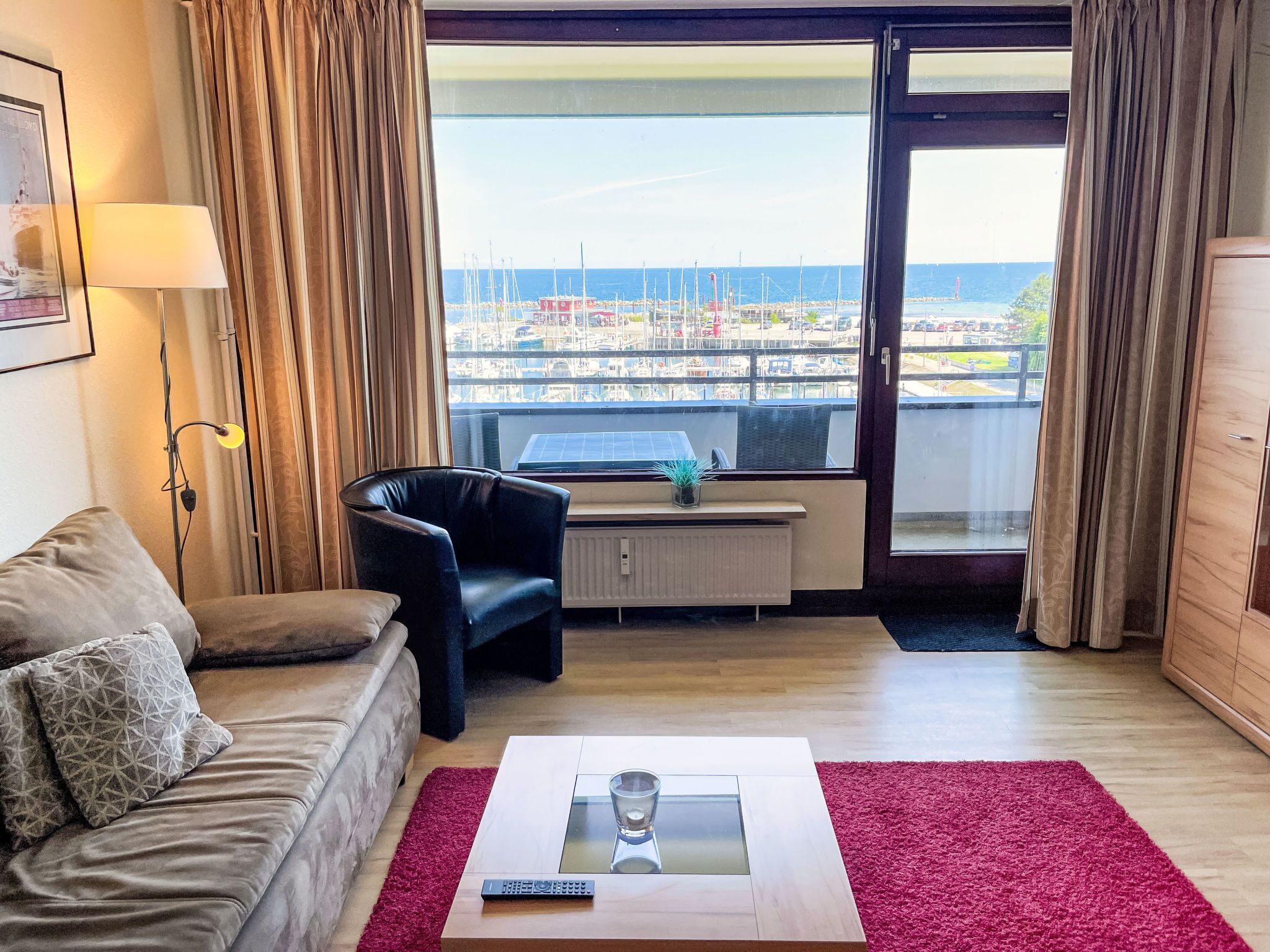 A modern living room with a sofa, a chair, a coffee table, and a view of a marina through a large window.