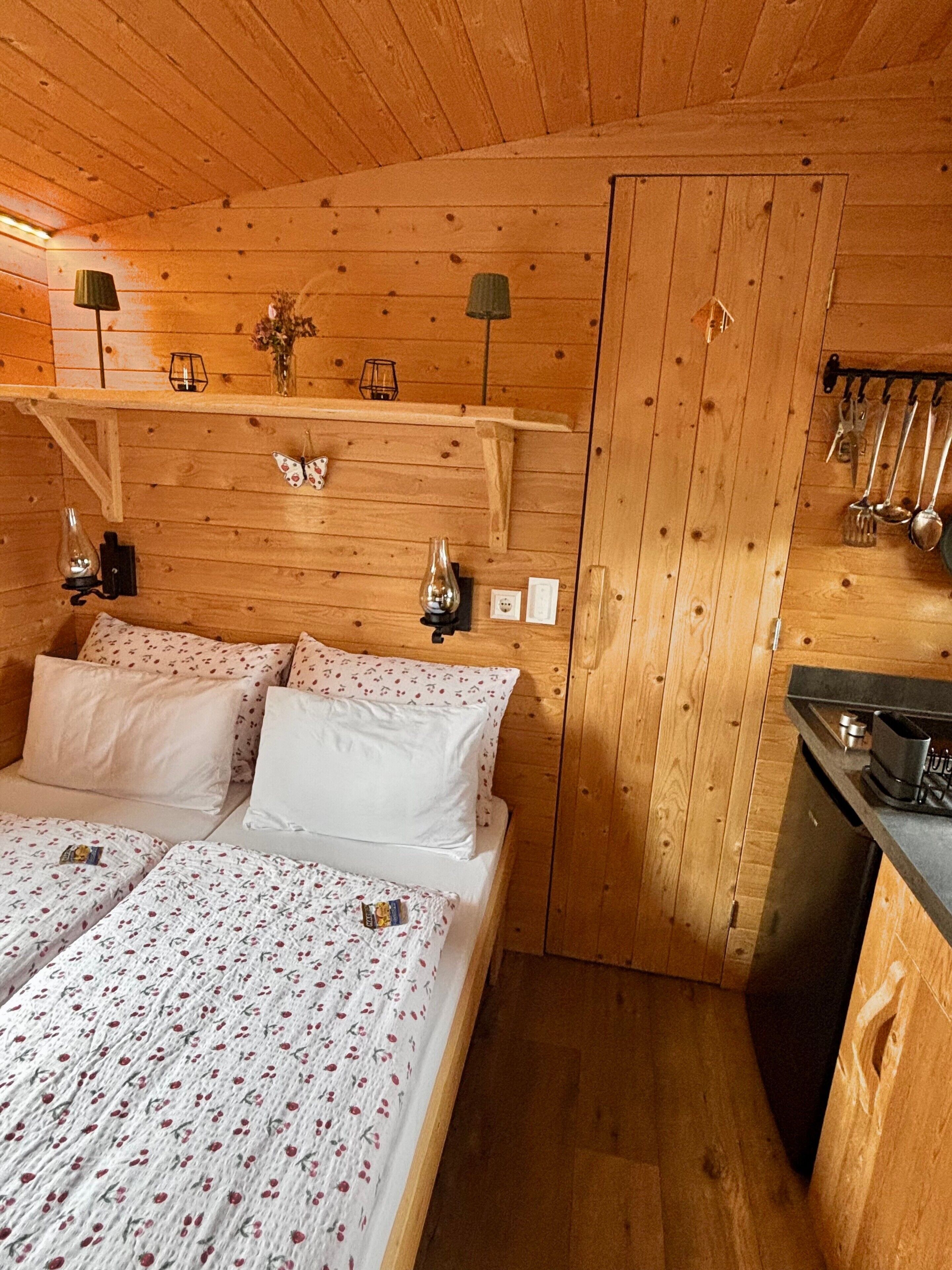 Un dormitorio de cabaña de madera con una cama, lámparas de noche, una mesita pequeña y un colgador para utensilios.