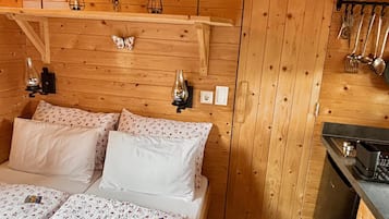 Un dormitorio de cabaña de madera con una cama, lámparas de noche, una mesita pequeña y un colgador para utensilios.