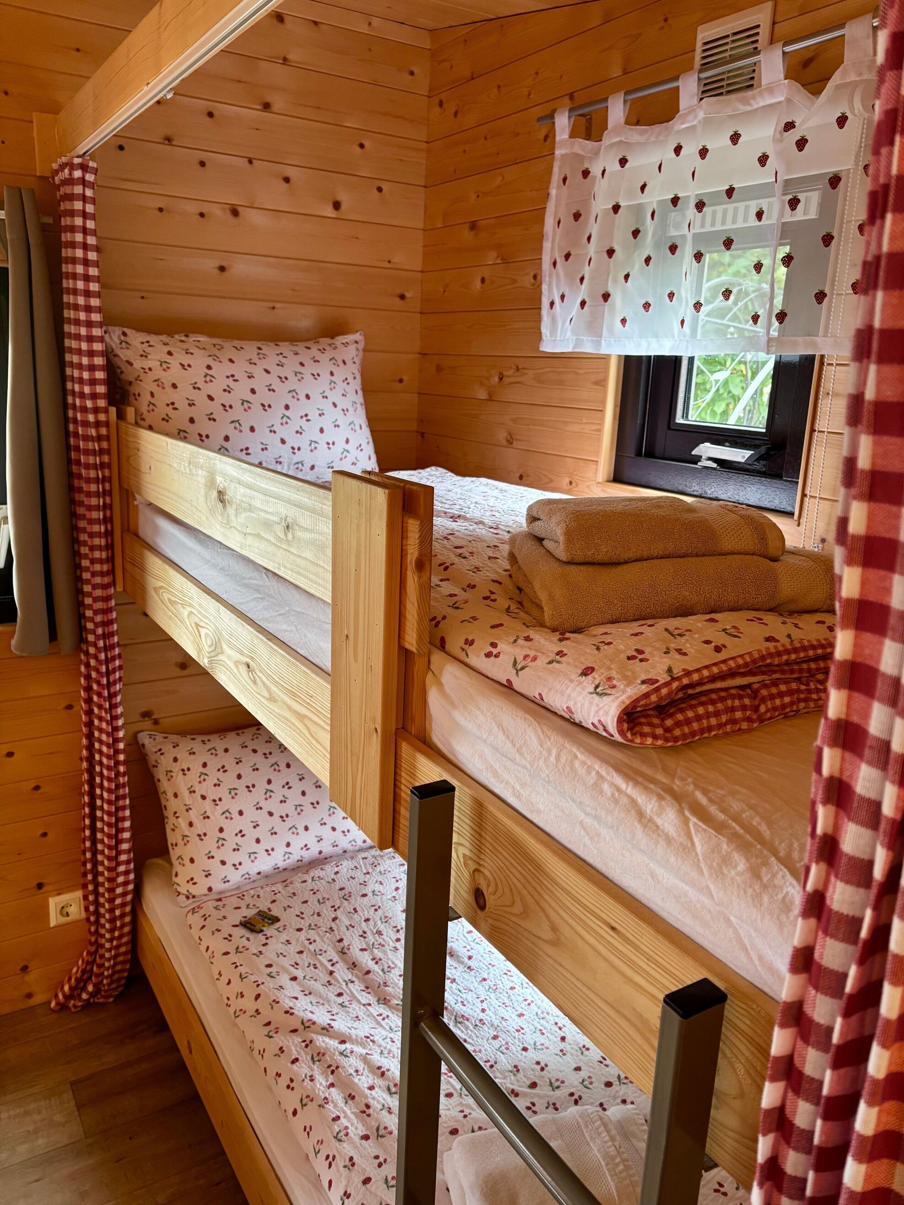 A bunk bed room with a window, wooden walls, and a checkered curtain.
