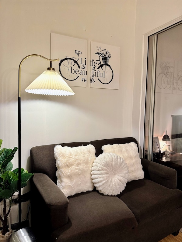 Una sala de estar moderna con un sofá, cojines decorativos, una lámpara de pie y cuadros en la pared.