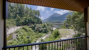 Vista de uma varanda com guarda-corpo de metal, sobre um rio, vegetação densa e uma ponte ao longe.