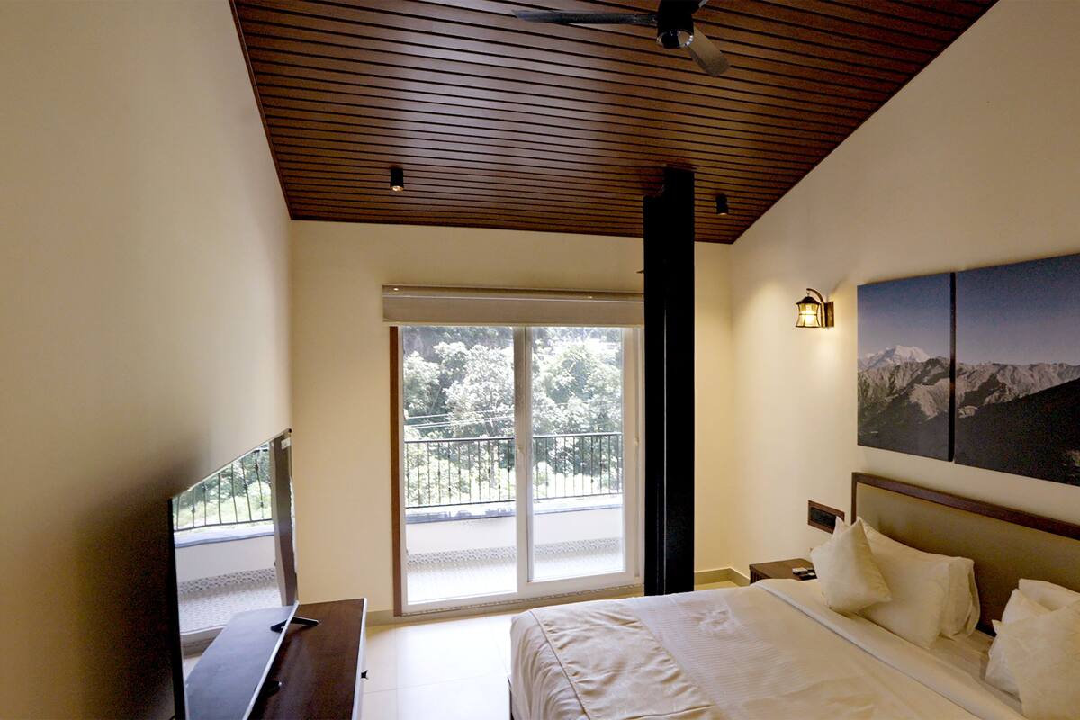 A bedroom with a bed, a nightstand, a wall-mounted TV, a window with a view of trees, and a ceiling with wooden slats.