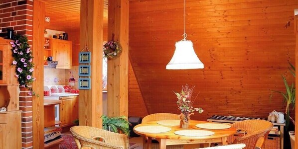 A cozy wooden interior with a round dining table, wicker chairs, and a hanging light fixture.