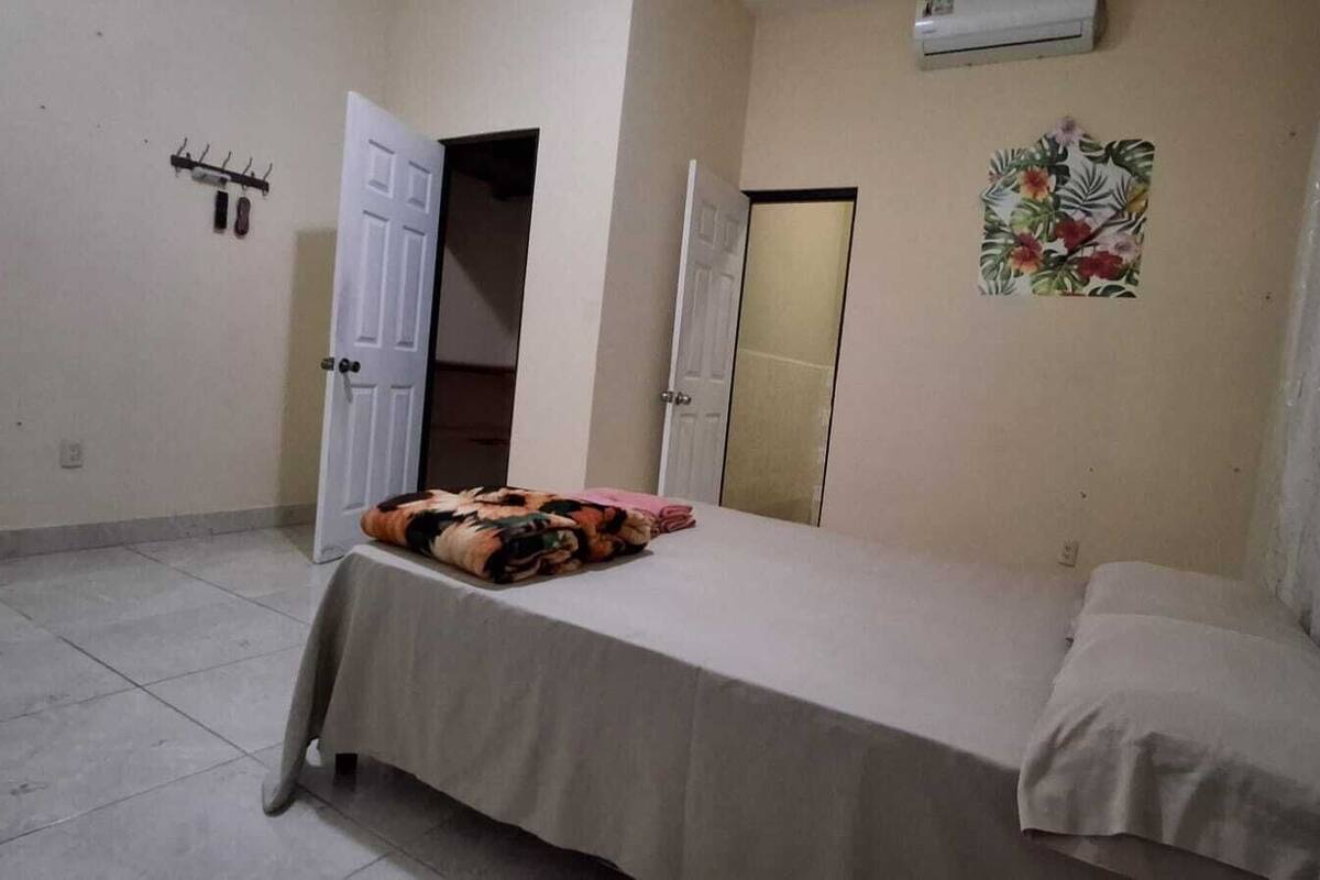 Quarto pequeno e limpo, com uma cama, uma porta e ar condicionado fixado na parede.
