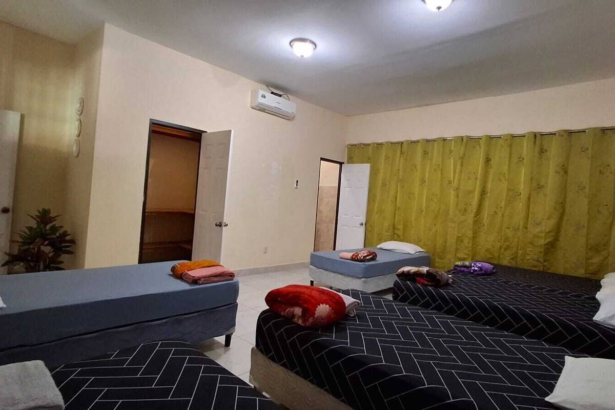 Quarto de hotel com duas camas de solteiro, um sofá pequeno, uma escrivaninha e uma porta que dá para outro quarto.