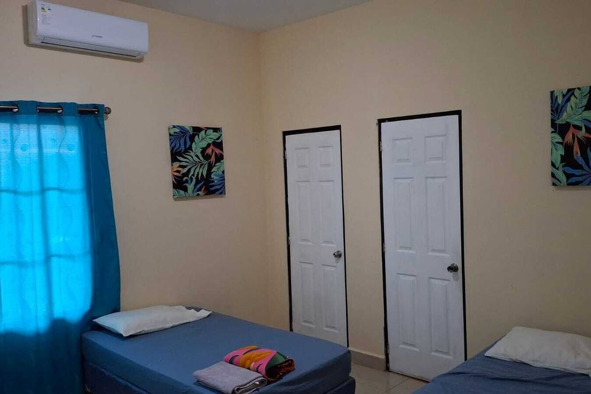 Quarto com duas camas, uma janela com cortinas azuis e duas portas.
