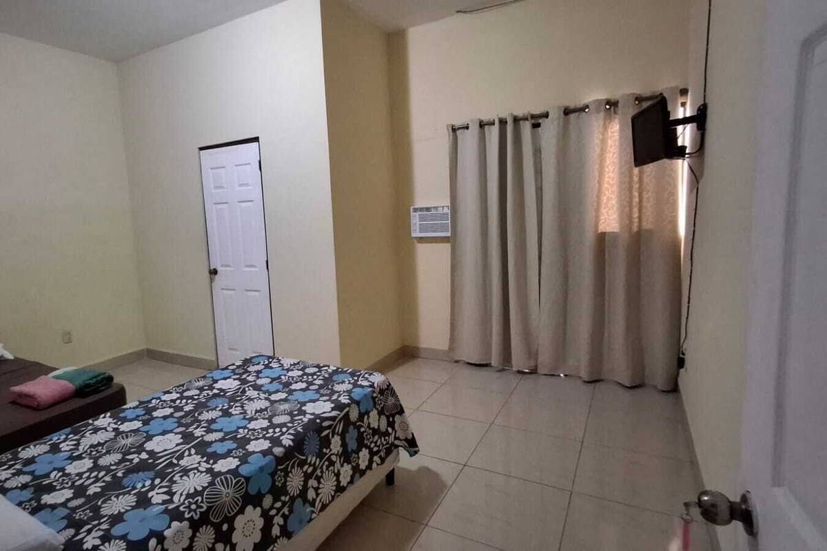 Um quarto com uma cama, mesa de cabeceira, guarda-roupa e cortina.