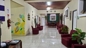 A hotel lobby with a reception desk, red seating, a green wall mural, and a dining area in the background. - Hostal Casa Habana  (Managua)