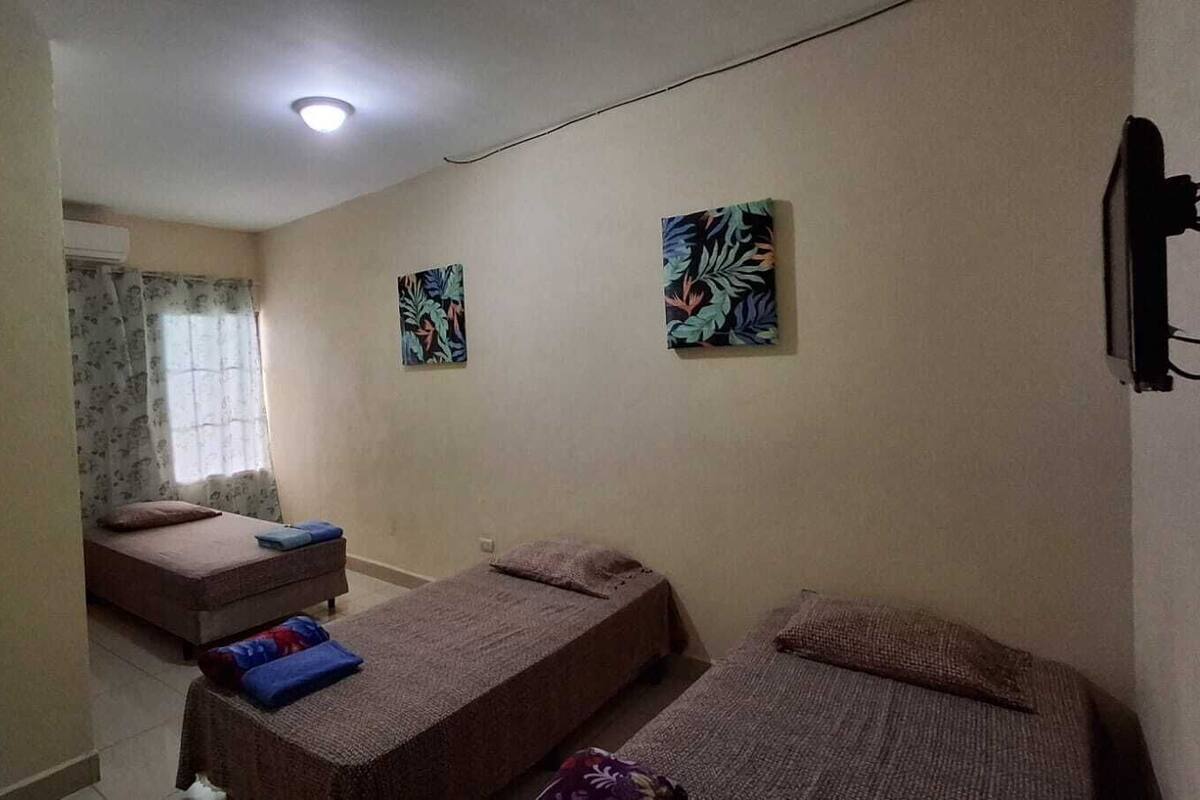 Quarto com duas camas de solteiro, uma mesinha e uma janela com cortinas.