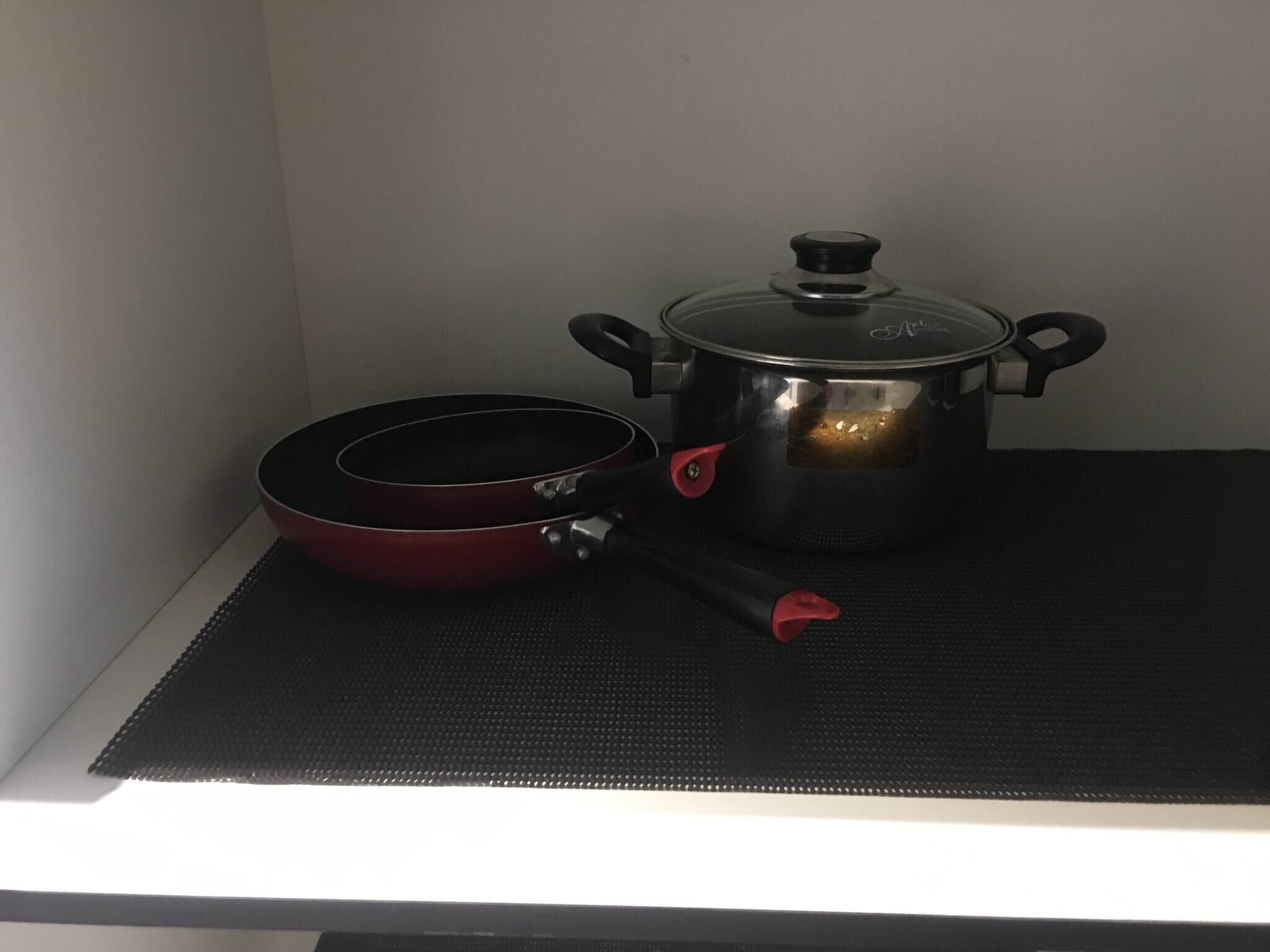 Een keuken met een fornuis, een rode pan en een roestvrijstalen pan met deksel.