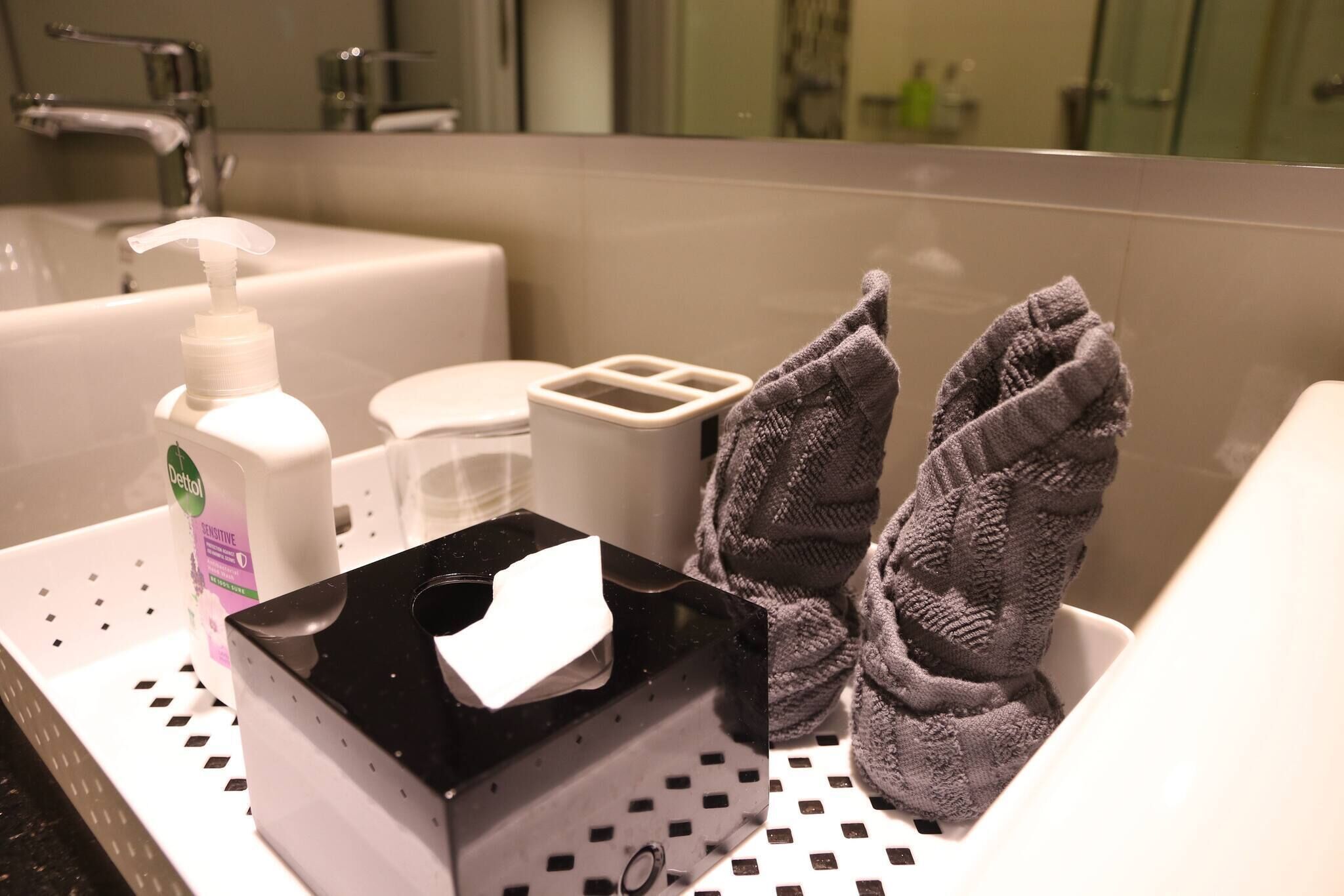 Un bagno con un lavandino, una bottiglia di sapone Dettol, un box di fazzoletti e un portascopevoli con asciugamani.