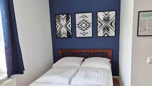 A bedroom with a wooden bed, a blue accent wall, and three patterned wall hangings. - Studio 1 - Apartments at the castle (Oberschleißheim)