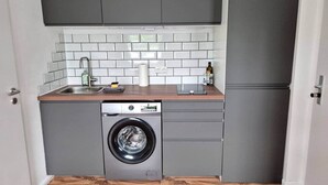 A compact kitchen with grey cabinets, a washing machine, and a refrigerator. - Studio 1 - Apartments at the castle (Oberschleißheim)