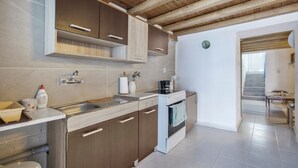 A kitchen with wooden cabinets, a sink, a stove, and a countertop with various kitchen items. - Description of Villa Sissy (Κεραμε)