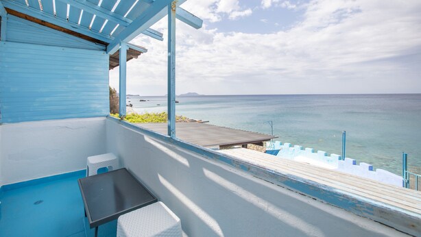 A balcony with a view of the sea, a wooden deck, and a covered seating area. - Description of Villa Sissy (Κεραμε)