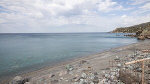 A coastal beach scene with clear water, rocky shore, and a construction site with metal scaffolding. - Description of Villa Sissy (Κεραμε)